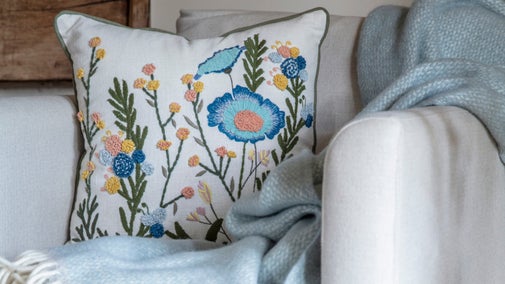 An embroidered cushion and light blue throw on a white chair